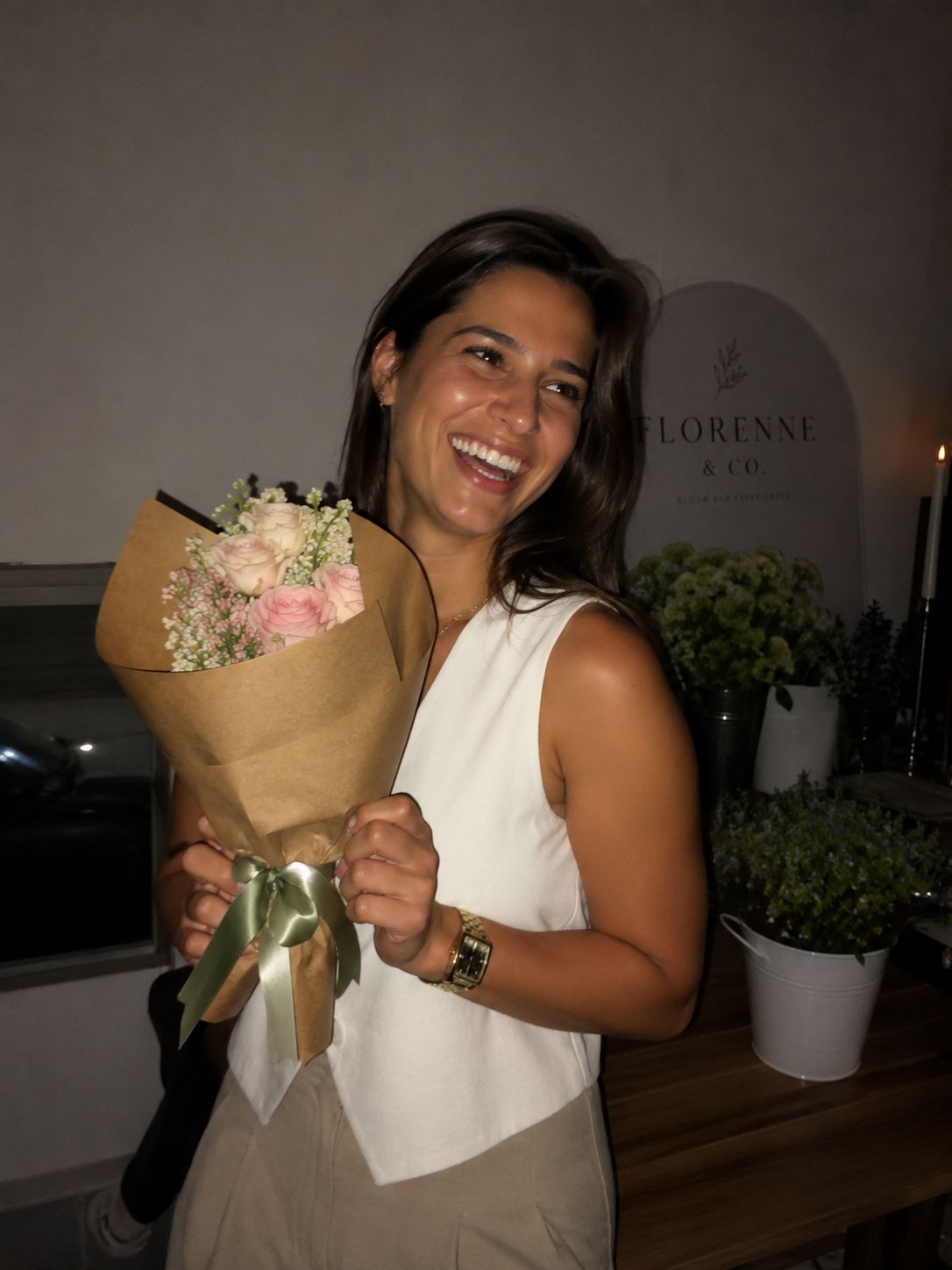 A guest holding a kraft-wrapped bouquet finished with a sage ribbon in front of the Florenne & Co. sign