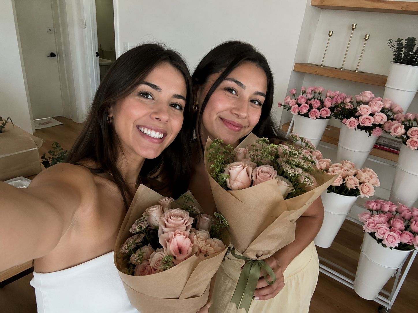Two friends photographing themselves with the bouquets they made, flower buckets behind them